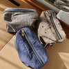 Trois pochettes de rangement cosmétique en tissu à motifs carreaux gris, marron et bleu sont présentées sur une surface en bo