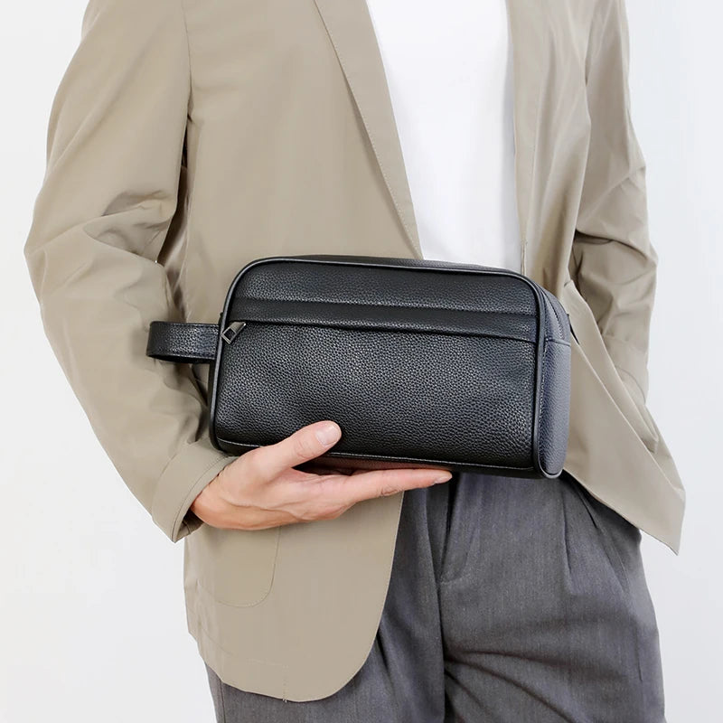 A black PU leather crossbody bag is held by a person wearing a beige blazer and gray pants.