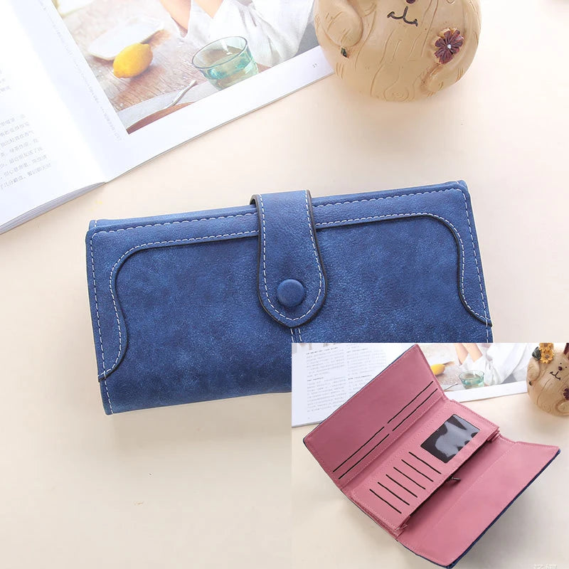 A navy blue PU leather clutch wallet with a flap and stitching is shown next to an open notebook and a small wooden toy.