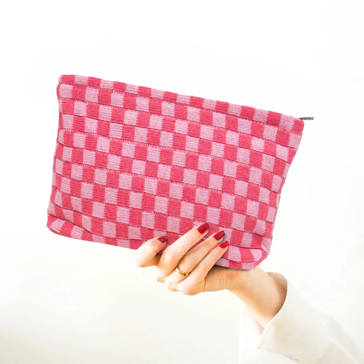 A hand holds a pink checkered makeup bag, showing the texture and color of the fabric.