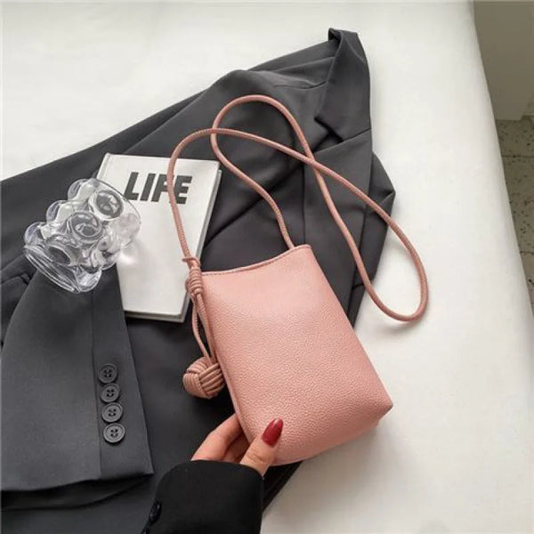 A pink leather crossbody bag with a tan strap is shown next to a white card on a gray blazer.
