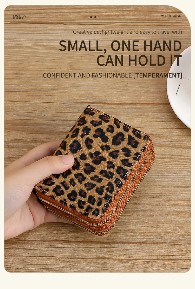 A hand holds a small leopard print wallet with an orange trim on a wooden surface.
