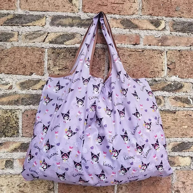 A purple reusable shopping bag featuring a pattern of small cats on a white background, displayed against a brick wall.