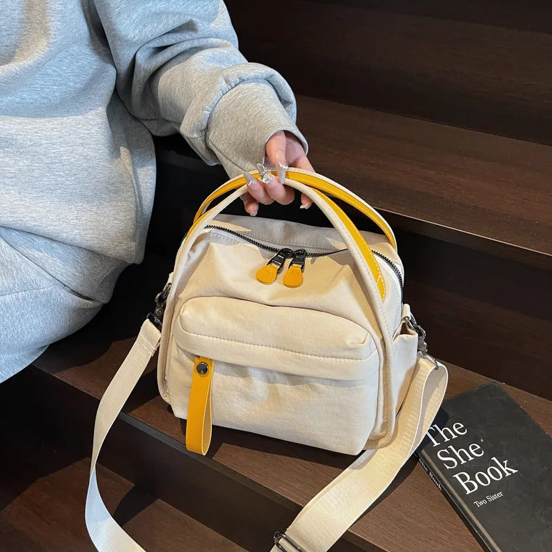 A beige nylon crossbody bag with a yellow top handle resting on a dark wooden surface.