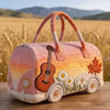 A quilted travel duffle bag in soft peach and orange tones with a wooden guitar design set against a golden field background.