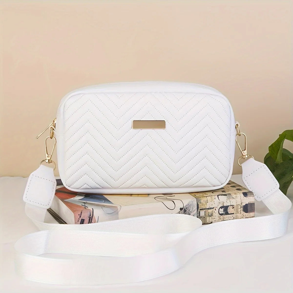 Weiße gesteppte Crossbody-Tasche mit goldfarbenen Beschlägen auf einer hellen Oberfläche.