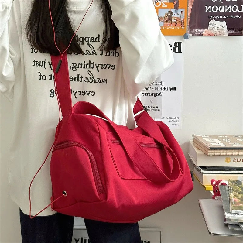 A bright red canvas crossbody travel tote bag is shown against a white shirt.