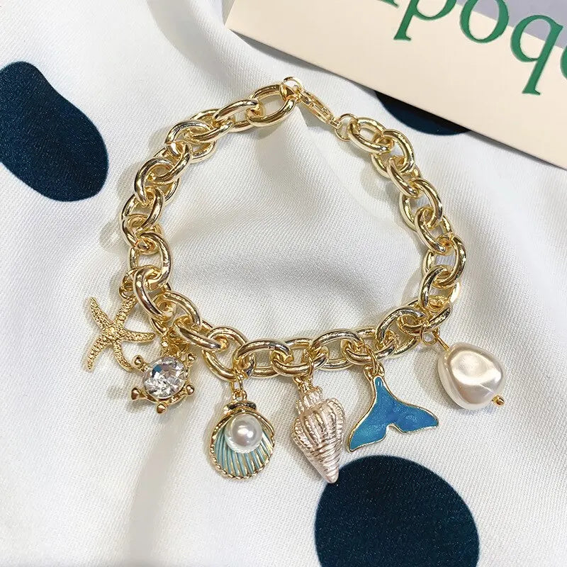 Gold chain bracelet featuring an ocean pearl charm, starfish, and shell accents.