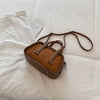 A brown retro crocodile textured mini crossbody bag resting on a white fabric with a small card.