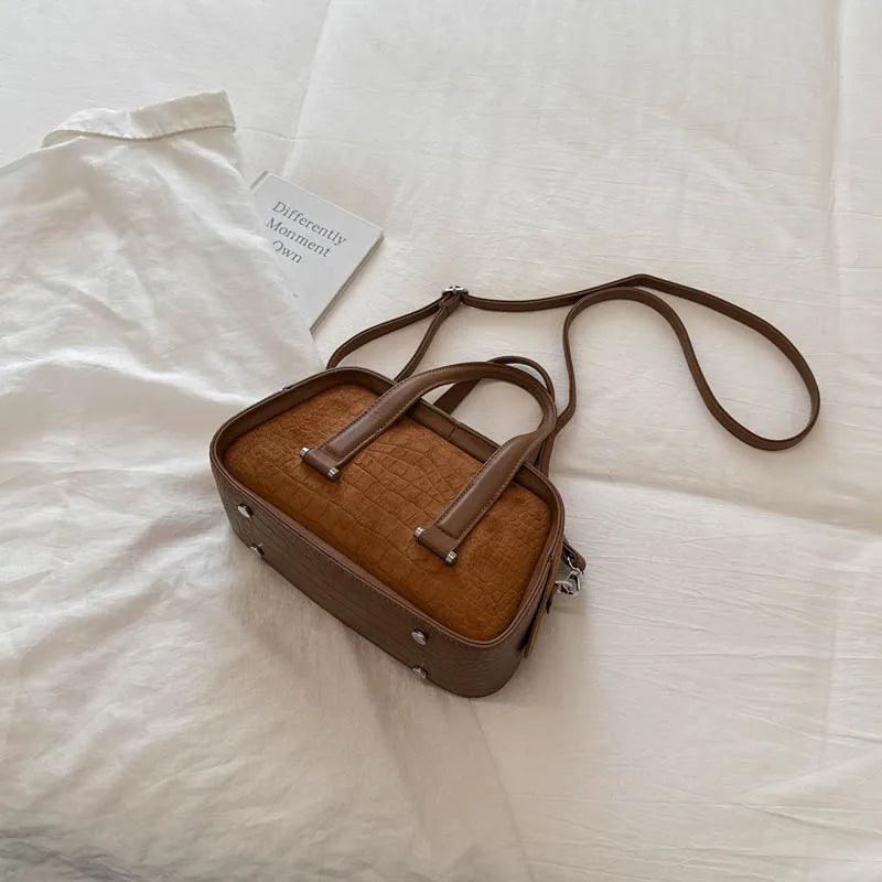 A brown retro crocodile textured mini crossbody bag resting on a white fabric with a small card.