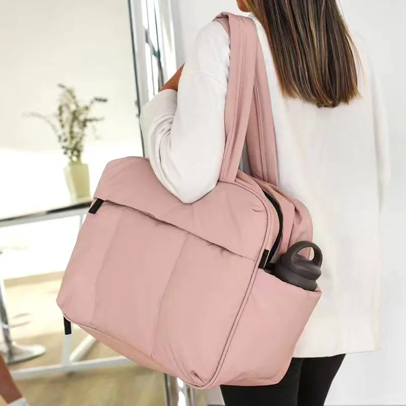 A woman is carrying a large pink travel duffle bag over her shoulder.