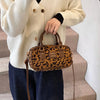 Eine Frau hält eine braune Leopardenmuster-Designer-Hobo-Tasche vor einem hellbeigen Pullover und dunkelblauen Hosen.