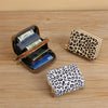 A leopard print PU leather compact wallet with a gold-toned zipper and a matching patterned clutch displayed on a wooden surf