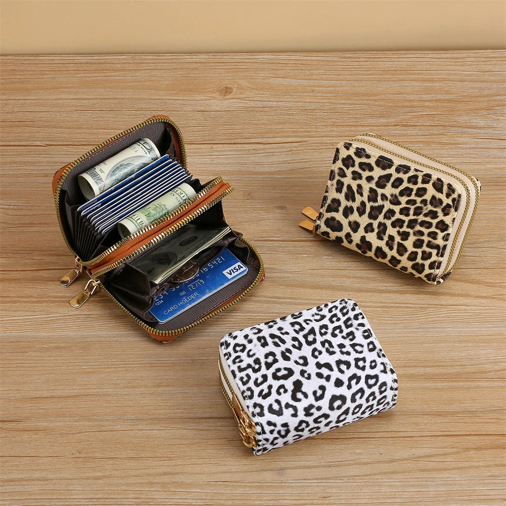 A leopard print PU leather compact wallet with a gold-toned zipper and a matching patterned clutch displayed on a wooden surf