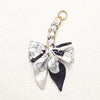 A white and black floral patterned fabric bow attached to a gold chain strap extension.