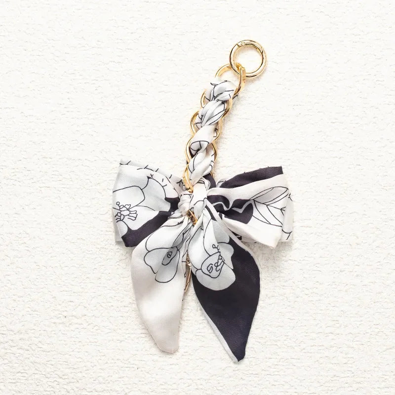 A white and black floral patterned fabric bow attached to a gold chain strap extension.