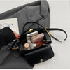 A black textured leather shoulder bag is shown open, revealing interior compartments and accessories against a gray suit jack