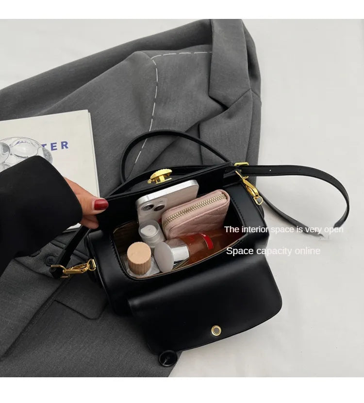 A black textured leather shoulder bag is shown open, revealing interior compartments and accessories against a gray suit jack
