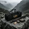 A black storage tote filled with tools rests on a large rock, surrounded by various outdoor gear and knife accessories.