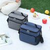 A navy blue insulated thermal lunch bag resting on a white surface with apples and a small pastry.
