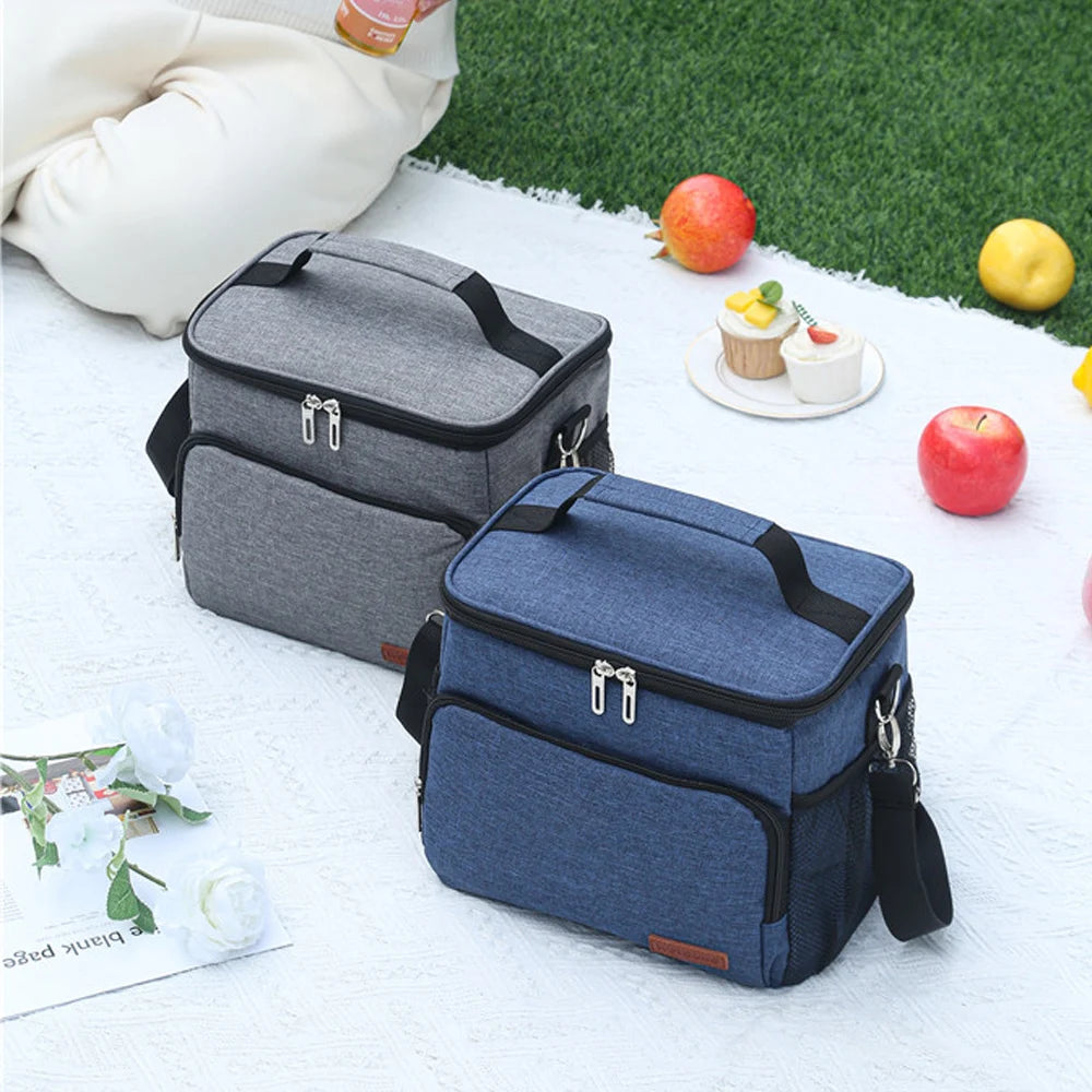 A navy blue insulated thermal lunch bag resting on a white surface with apples and a small pastry.