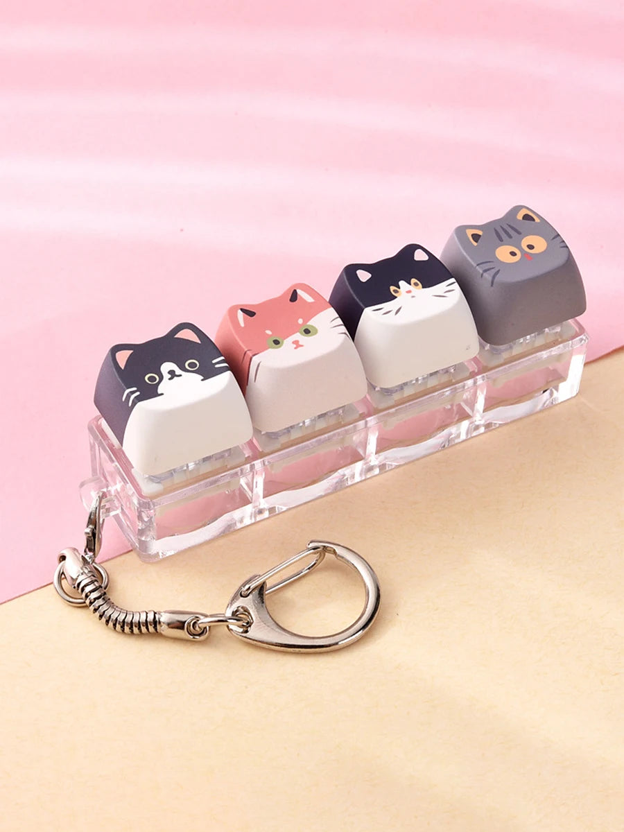 A set of nine acrylic cat keycaps in various colors and shades displayed on a clear plastic tray with a silver bag charm.