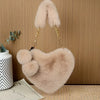 A light beige faux fur heart-shaped crossbody purse with gold hardware displayed on a wooden surface.