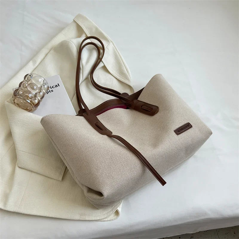 A beige canvas shoulder tote bag with brown leather straps and a small tag resting on the fabric.
