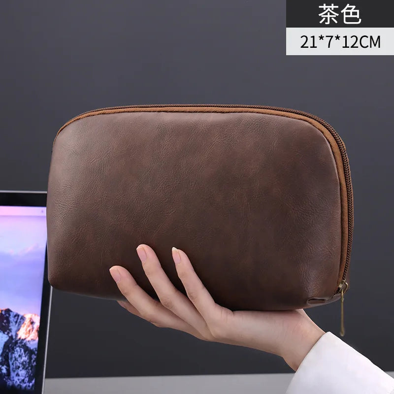 A brown leather multi-layer cable organizer pouch is held in a hand, showing its size and texture.