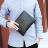A man wearing a light gray shirt holds an elegant black PU leather men's clutch wallet.