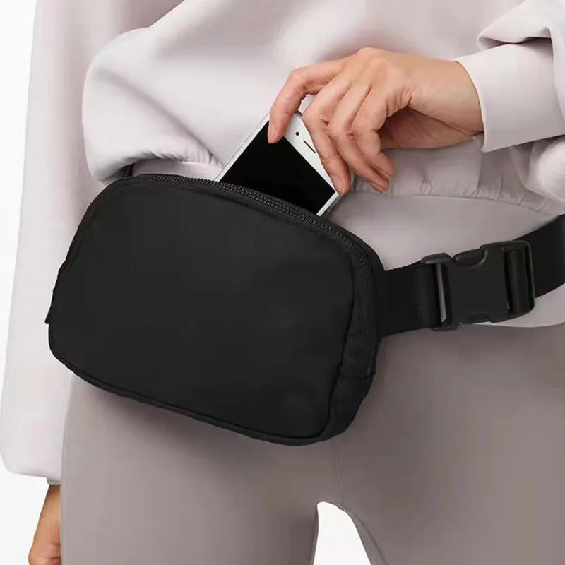 A black waist bag is worn by a woman, featuring a strap and designed to hold a smartphone.
