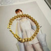 A close-up of a gold stainless steel charm bracelet featuring a portrait pendant.