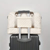 A beige durable nylon travel duffle bag with silver handles resting on a gray suitcase.