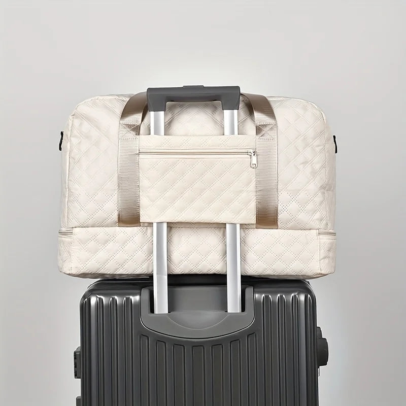 A beige durable nylon travel duffle bag with silver handles resting on a gray suitcase.