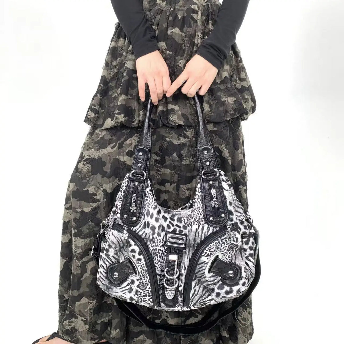 A woman wearing a dark camouflage outfit holds a black leopard print crossbody shoulder bag.