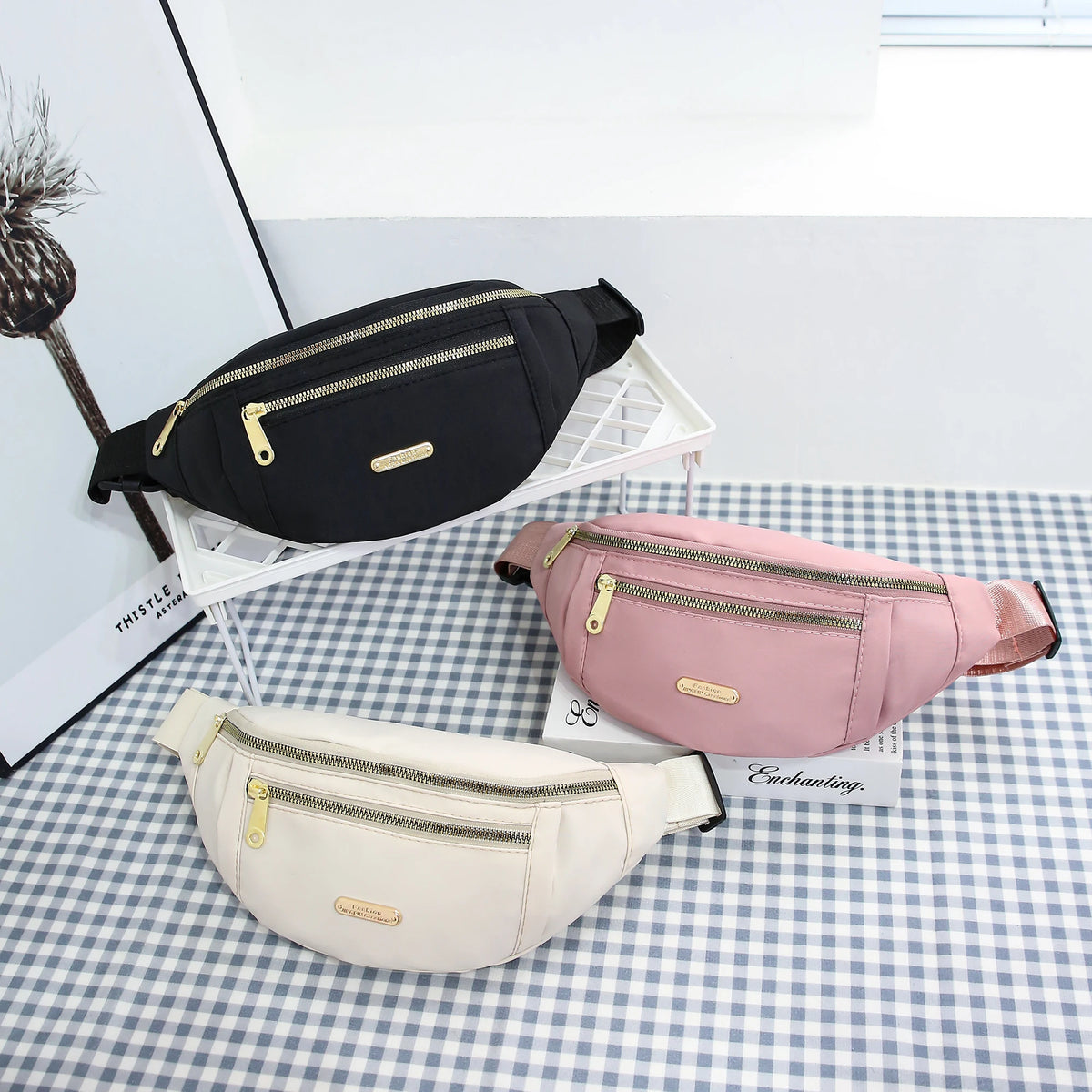 A pink multi-layer sports waist bag is displayed on a checkered surface next to a black one.