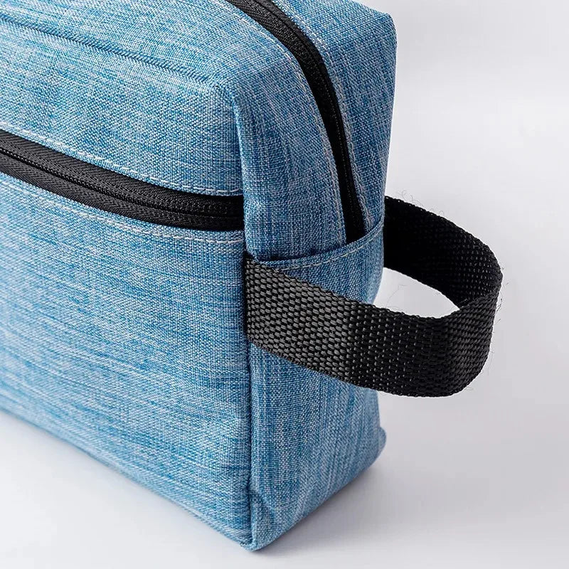 A light blue fabric travel cosmetic bag with black trim and a black strap.
