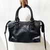 A hand holds a black soft PU leather shoulder tote bag with a curved handle and leather strap.