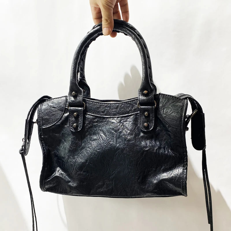 A hand holds a black soft PU leather shoulder tote bag with a curved handle and leather strap.