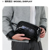 A black crocodile print clutch bag is displayed in a model's hand against a gray blazer.