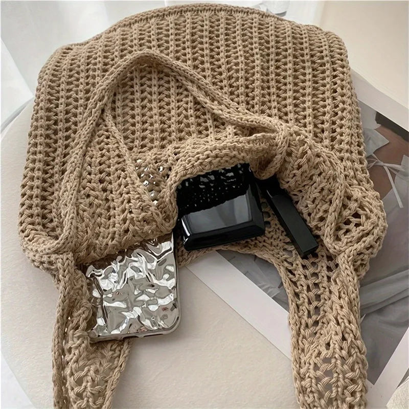 A beige knit shoulder bag with a bohemian texture is displayed on a white surface, featuring a black accessory.