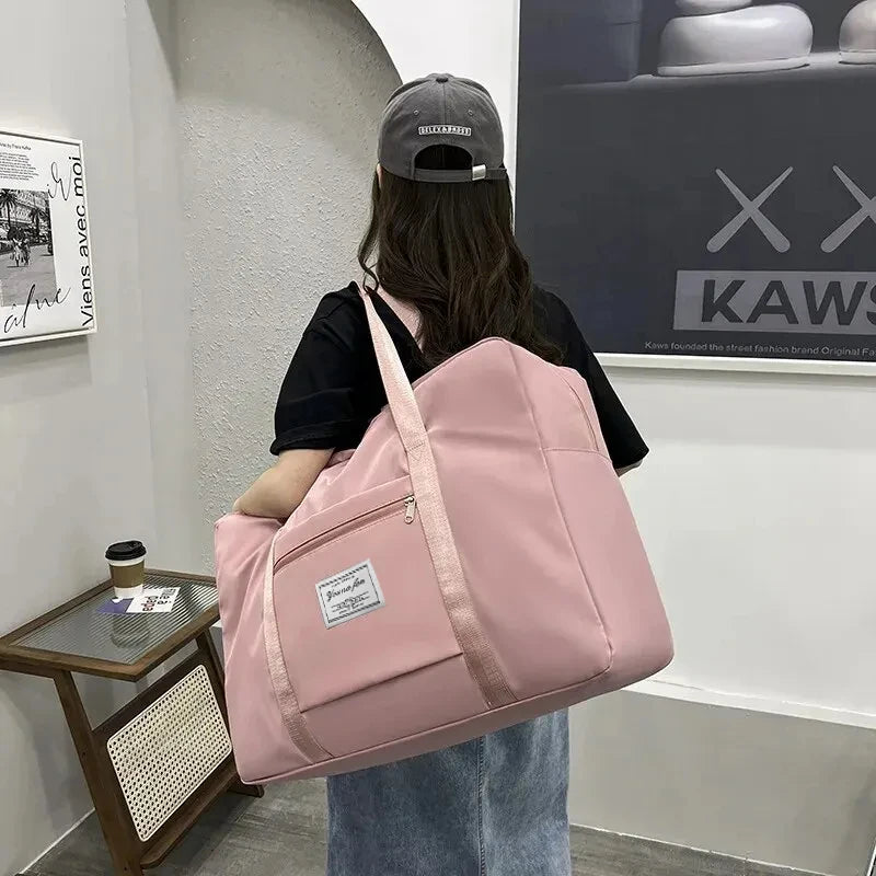 A person is holding a pink canvas travel storage bag with multiple compartments in front of a wall display.