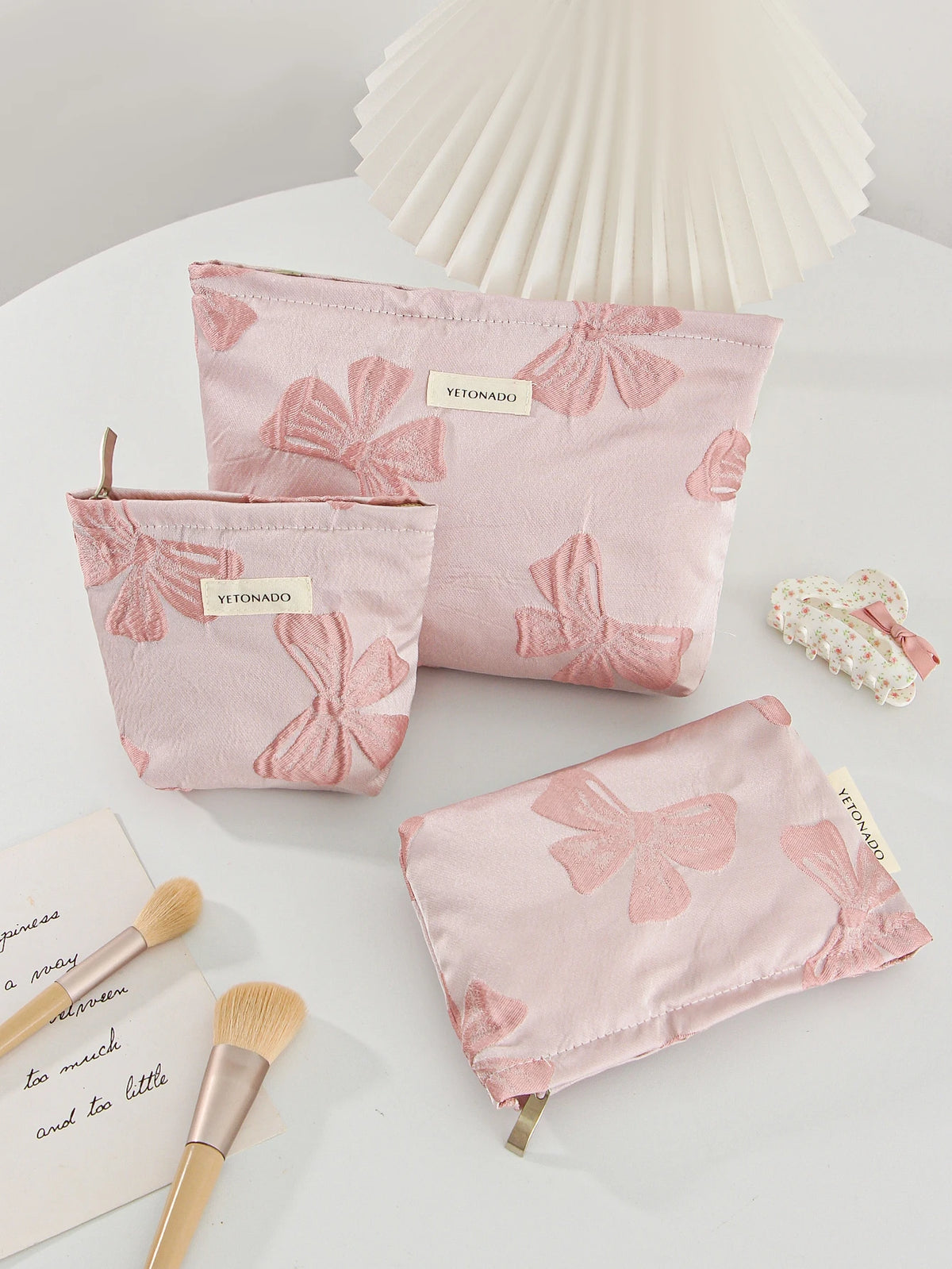 Pink bow knot cosmetic organizer bags and a large pink paper fan on a white surface.