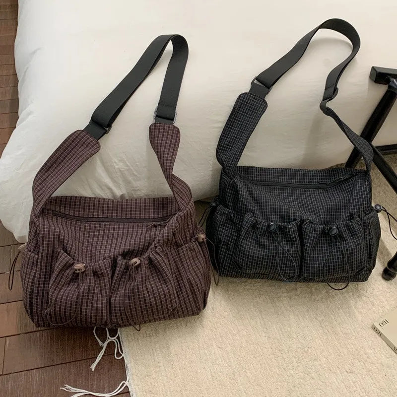A pair of plaid nylon drawstring tote bags in brown and black checkered patterns resting on a light-colored surface.