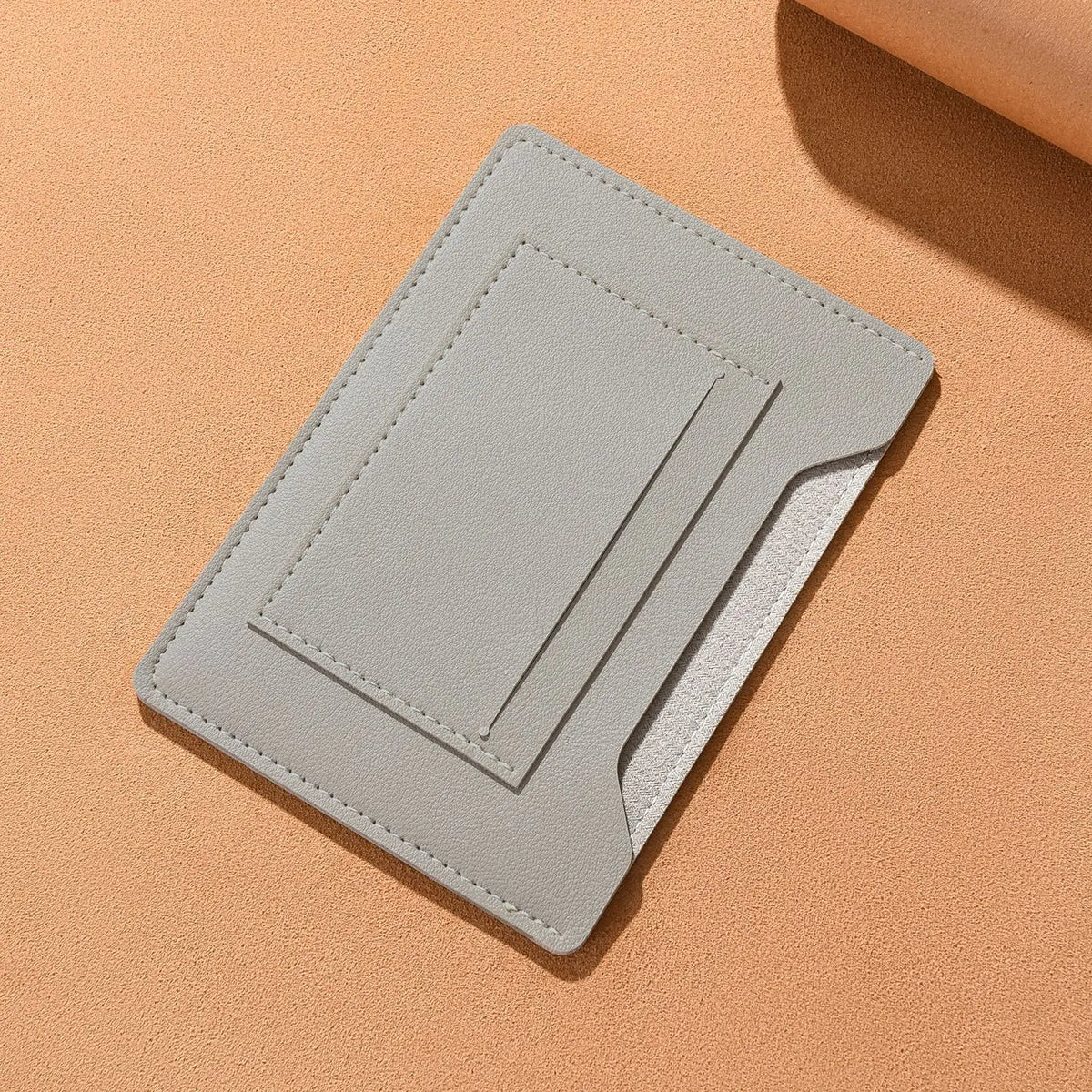 Portefeuille de voyage fin gris clair, plié et posé sur une surface douce couleur pêche.