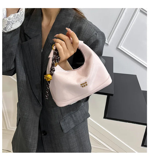 Hellrosa Retro-Leder-Schultertasche mit goldfarbenem Kettenriemen, gehalten von einer Frau in einem grauen Blazer.
