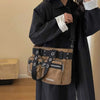 A woman wearing a black coat holds a tan nylon shoulder bag with black straps and metal hardware.