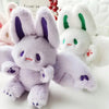 A soft purple and white bat bunny plush toy with large ears and wings is shown against a white background.