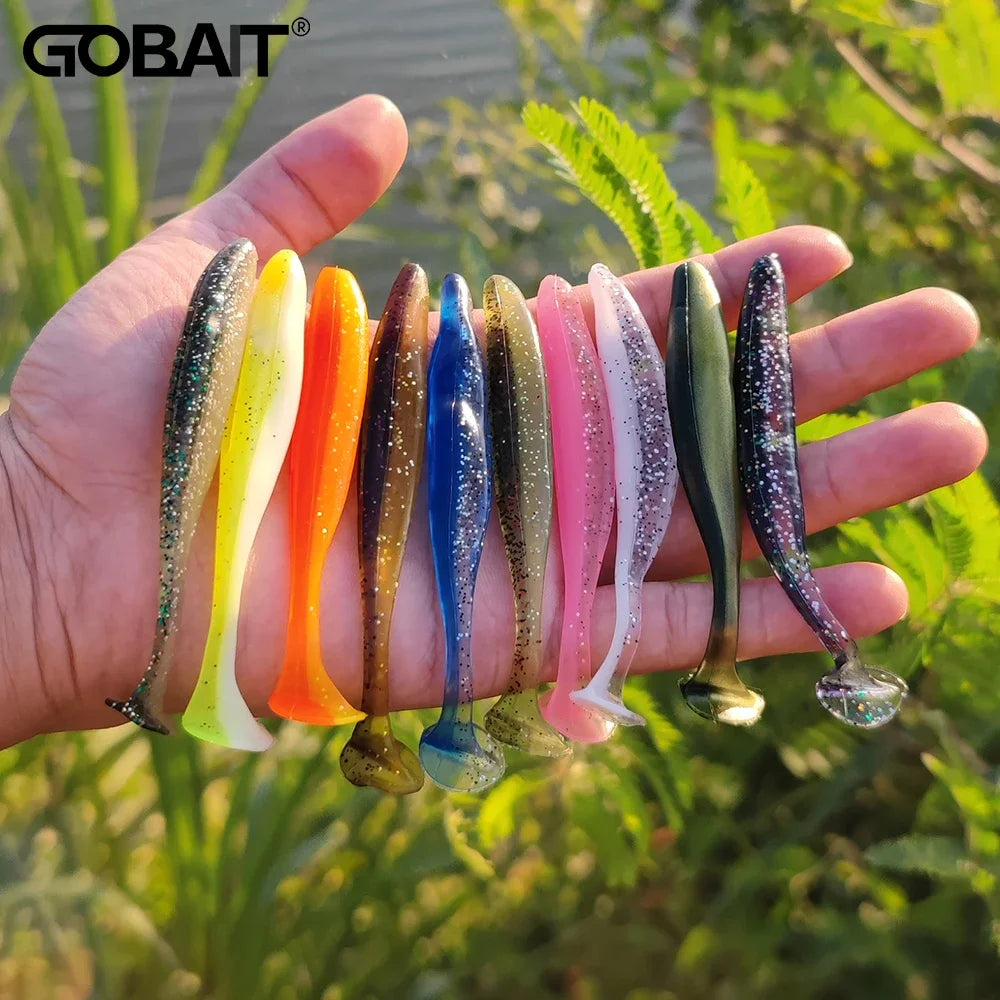 A hand holds a variety of colorful, adjustable soft lure fishing tackle baits.