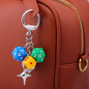 A silver keychain charm featuring three colorful dice attached to a leather suitcase zipper pull.